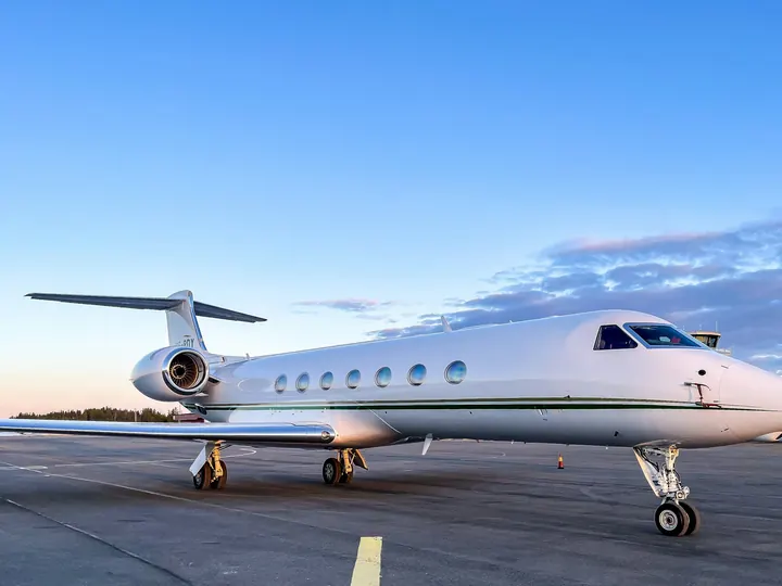 A large-cabin business jet on a runway under a bright blue sky