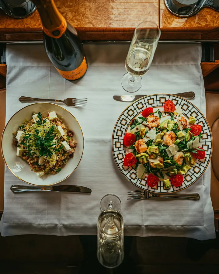 A plated meal and white wine on a dining table aboard a private jet, seen from above