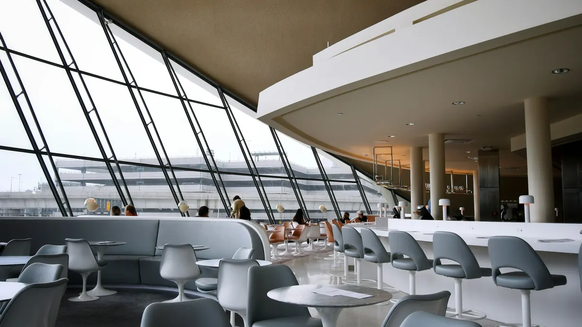 A quiet airport lounge with tall windows and white chairs