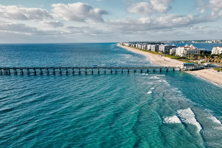 Aerial view of a pier reaching into turquoise water off Palm Beach